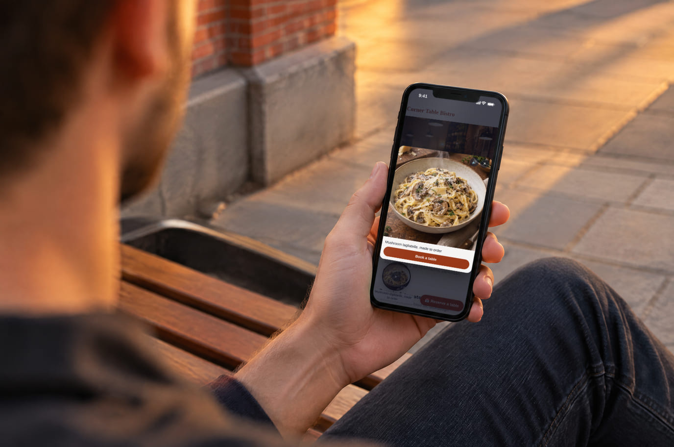 A guest on a city bench watches a dish clip from the bistro website on his phone while choosing where to have dinner